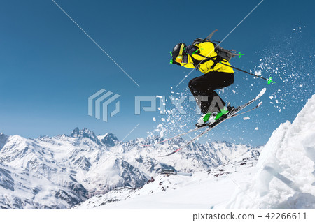 A skier in full sports equipment jumps into the precipice from the top of the glacier against the A skier in full sports equipment jumps into the precipice from the top of the glacier against the 42266611
