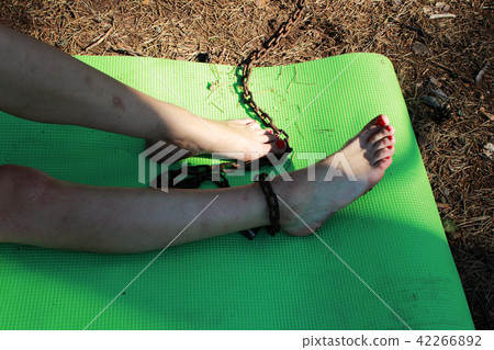The leg of a girl, chained to a tree for a rusty chain. the concept of slavery, subordination and The leg of a girl, chained to a tree for a rusty chain. the concept of slavery, subordination and 42266892