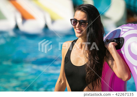 happy woman carrying rubber ring near pool and slides happy woman carrying rubber ring near pool and slides 42267135