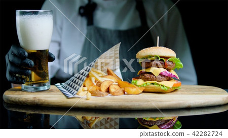 Chef is serving set of tasty burger, french fries and beer on the wooden tray on the black 42282724