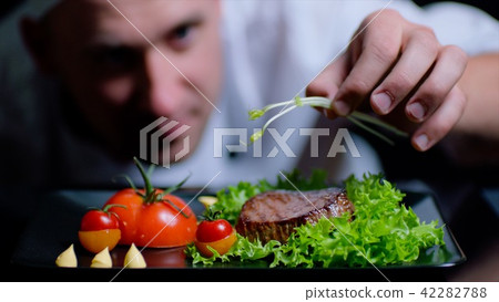 Chef is finishing the delicious beef dish with greens. Chef is out of focus on the background 42282788