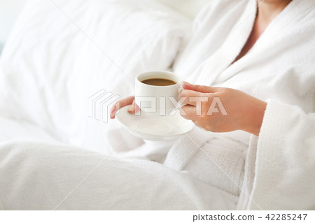 Woman wearing white robe with cup of coffee Woman wearing white robe with cup of coffee 42285247