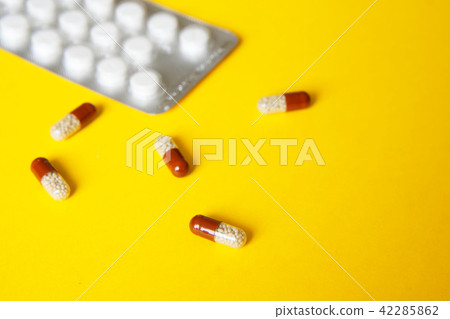 Blister with pills and capsules on a yellow Blister with pills and capsules on a yellow 42285862