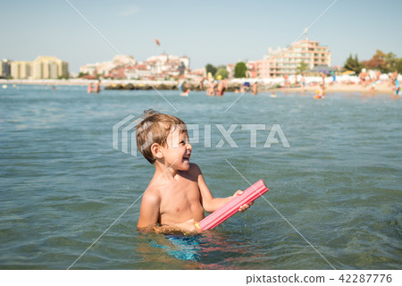 Joyful little boy shoots from a water-pistol at someone in the sea Joyful little boy shoots from a water-pistol at someone in the sea 42287776