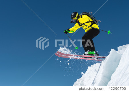 A skier in full sports equipment jumps into the precipice from the top of the glacier against the 42290700