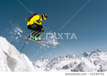 A skier in full sports equipment jumps into the precipice from the top of the glacier against the A skier in full sports equipment jumps into the precipice from the top of the glacier against the 42290702