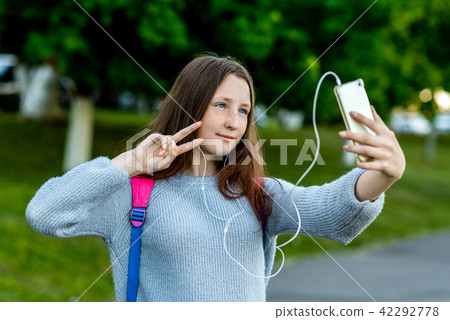 Girl schoolgirl student, in summer after school in nature. In his hands holds a smartphone, listen Girl schoolgirl student, in summer after school in nature. In his hands holds a smartphone, listen 42292778