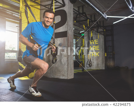 Cheerful man doing workout with suspension cable Cheerful man doing workout with suspension cable 42294875