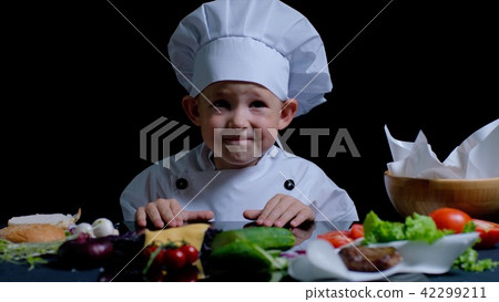 Little boy is cooking at the kitchen, he is wearing chefs suit 42299211