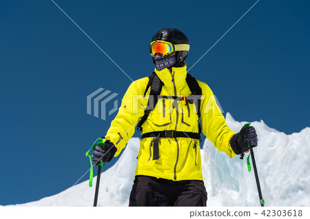 Skier standing on a slope. Man in a light suit, the helmet and mask in skiing is to ski. In the Skier standing on a slope. Man in a light suit, the helmet and mask in skiing is to ski. In the 42303618