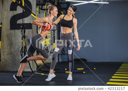 Cheerful girl is using trx straps with instructor Cheerful girl is using trx straps with instructor 42313217