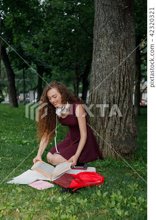 girl student holding book and sitting under tree 42320321