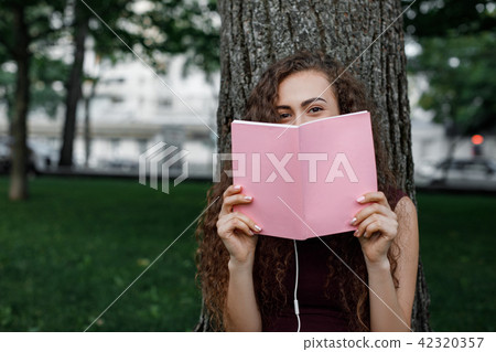 girl student holding book and sitting under tree 42320357