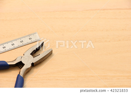 A metal ruler (straight length) placed on a wooden plate and pliers 42321833