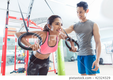 Beautiful young woman smiling while doing push-ups on gymnastic rings 42324329