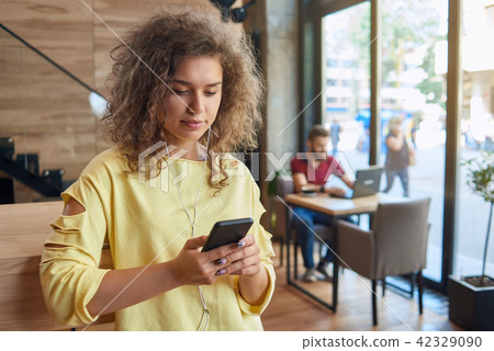 Front view of curly student wearing yellow blouse listening to music. 42329090