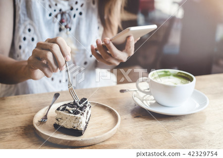 Young woman using smart phone and eating cake 42329754