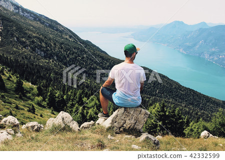Young man sitting on the hill top and enjoying valley view. Succes, vacation and travel concept 42332599