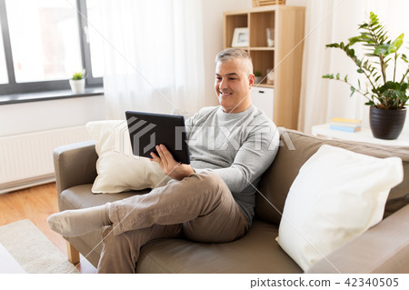 man with tablet pc sitting on sofa at home 42340505