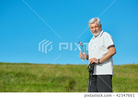 Old man keeping water bottle and tracking sticks. 42347601
