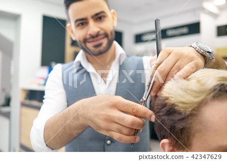 Doing new hairstyle for male model using sharp metallic scissors. 42347629
