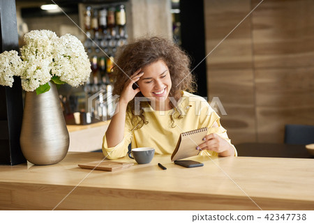 Fancy laughing young girl sitting on wooden table keeping blocknote. Fancy laughing young girl sitting on wooden table keeping blocknote. 42347738