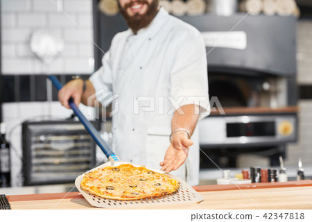 Cropped photo of baker holding fresh baked pizza laying on metallic shovel. Cropped photo of baker holding fresh baked pizza laying on metallic shovel. 42347818