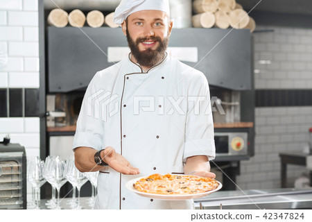 Smiling pizzaiolo holding fresh baked mouthwatering, delicious pizza. Smiling pizzaiolo holding fresh baked mouthwatering, delicious pizza. 42347824