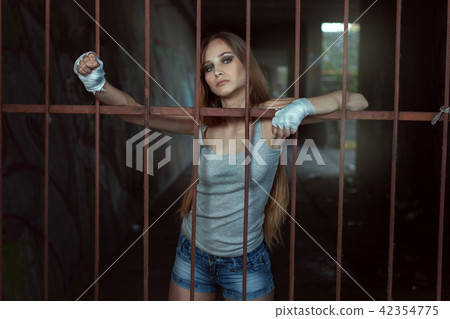 Young female fighter stands behind an iron fence. Young female fighter stands behind an iron fence. 42354775