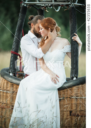 Happy lovely wedding couple bride and groom are sitting inside airballoon basket in the sunny field. Happy lovely wedding couple bride and groom are sitting inside airballoon basket in the sunny field. 42355638