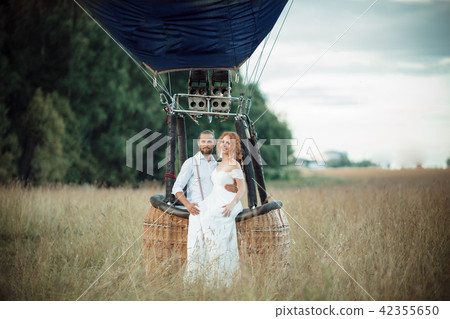 Happy wedding couple are sitting inside airballoon basket in the sunny field. 42355650