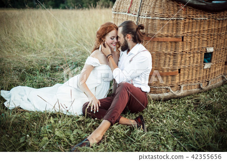 Happy wedding couple are sitting near airballoon basket in the sunny field. Happy wedding couple are sitting near airballoon basket in the sunny field. 42355656