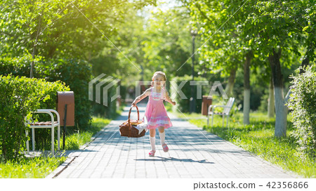 The girl runs along the road with a basket of bread. 42356866