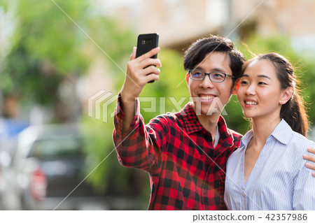Young happy Asian couple taking selfie together outdoors 42357986