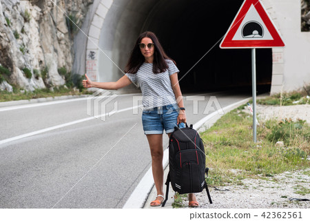 Young beautiful woman with black backpack hitchhiking standing near the road tunnel. 42362561