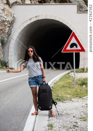 Young beautiful woman with black backpack hitchhiking standing near the road tunnel. Young beautiful woman with black backpack hitchhiking standing near the road tunnel. 42362562