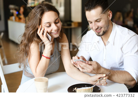Young nice woman talking by smartphone and sitting with man using hotspot at cafe. Young nice woman talking by smartphone and sitting with man using hotspot at cafe. 42377332