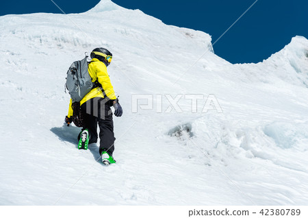 A skier in a helmet and mask with a backpack rises on a slope against the background of snow and a 42380789