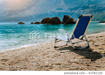 Beach chair from back on tranquil pebble beach. Amazing view to impressive rocks in the water Beach chair from back on tranquil pebble beach. Amazing view to impressive rocks in the water 42392140