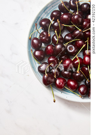 Freshly picked cherries on a half of blue plate on gray concrete background. Colorful organic 42392150