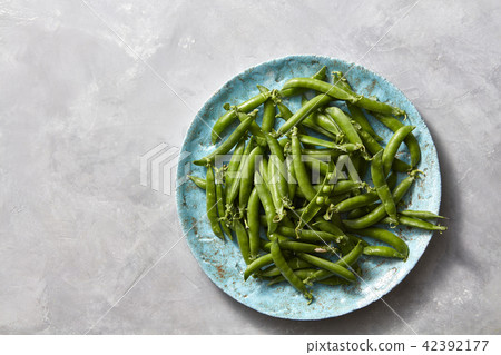 Natural organic green peas in sticks on a blue ceramic plate on a gray marble kitchen table. Top Natural organic green peas in sticks on a blue ceramic plate on a gray marble kitchen table. Top 42392177