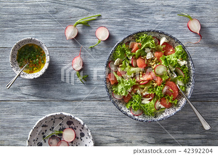 Fresh spring salad with radish, tomatoes, greens in ceramic bowl on gray wooden table. Flat lay. Fresh spring salad with radish, tomatoes, greens in ceramic bowl on gray wooden table. Flat lay. 42392204