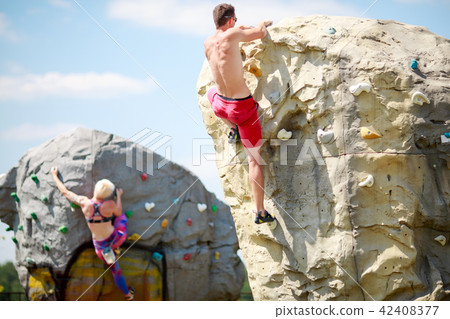 Photo from back of young athlete man in red shorts and woman on workout at climbing boulders against Photo from back of young athlete man in red shorts and woman on workout at climbing boulders against 42408377