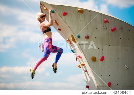 Photo from side of sports blonde in leggings hanging on wall for climbing against blue sky 42408404