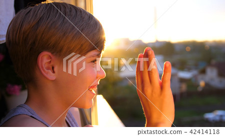 Young guy standing by the window in the morning. The first rays of the sun illuminate the room. The 42414118