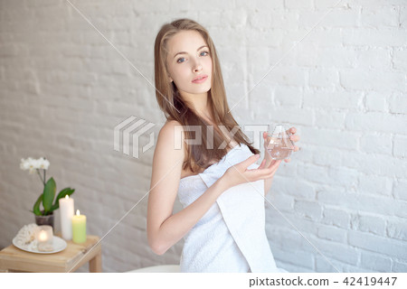 Caucasian smiling woman after spa covered with white towel holding a glass of water Caucasian smiling woman after spa covered with white towel holding a glass of water 42419447