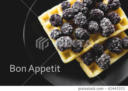 Belgian waffles with frozen blackberries on a black background, inscription bon appetit Belgian waffles with frozen blackberries on a black background, inscription bon appetit 42443353
