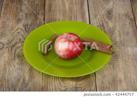 Red apple and cinnamon in a green plate 42444757