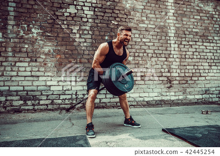 Athletic man working out with a barbell. Strength and motivation. Exercise for the muscles of the Athletic man working out with a barbell. Strength and motivation. Exercise for the muscles of the 42445254