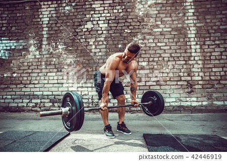 Athletic man working out with a barbell. Strength and motivation. Exercise for the muscles of the Athletic man working out with a barbell. Strength and motivation. Exercise for the muscles of the 42446919